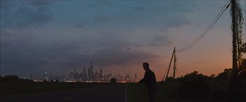 Movie still from “Looper” (2012), directed by Rian Johnson – A man standing on top of a grass covered field at night; Extreme Wide shot, Low angle