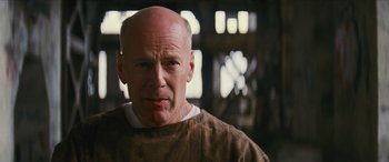 Movie still from “Looper” (2012), directed by Rian Johnson – A man with a shaved bald head wearing a brown shirt; Close Up shot, Low angle