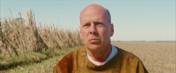 Movie still from “Looper” (2012), directed by Rian Johnson – A bald man in a brown shirt is looking at the camera; Close Up shot, Low angle