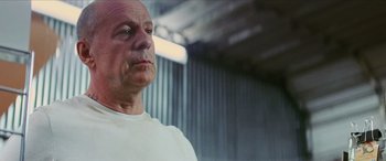 Movie still from “Looper” (2012), directed by Rian Johnson – A bald man in a white t - shirt is looking to his left; Close Up shot, Low angle