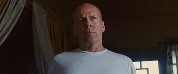 Movie still from “Looper” (2012), directed by Rian Johnson – A man with a bald head wearing a white t - shirt; Close Up shot, Low angle