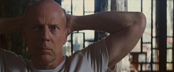 Movie still from “Looper” (2012), directed by Rian Johnson – A bald man with his arms behind his head; Close Up shot, Low angle