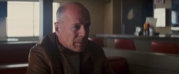 Movie still from “Looper” (2012), directed by Rian Johnson – A man with a bald head sitting at a table in a restaurant; Close Up shot, Low angle