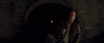 Movie still from “Looper” (2012), directed by Rian Johnson – A man holding a gun while standing next to a light; Medium shot, High angle