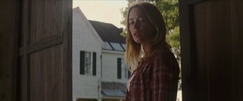 Movie still from “Looper” (2012), directed by Rian Johnson – A woman standing in front of a house looking out a window; Medium shot, Low angle