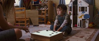 Movie still from “Looper” (2012), directed by Rian Johnson – A young boy sitting on the floor next to a wooden box; Medium shot, High angle