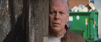 Movie still from “Looper” (2012), directed by Rian Johnson – A bald man with a white shirt and a brown jacket; Close Up shot, Low angle