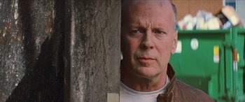 Movie still from “Looper” (2012), directed by Rian Johnson – A man with a beard is standing next to a wall; Close Up shot, Low angle