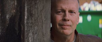 Movie still from “Looper” (2012), directed by Rian Johnson – A person's face near a tree trunk; Close Up shot, Low angle