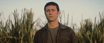 Movie still from “Looper” (2012), directed by Rian Johnson – A man in a brown jacket standing in front of a field; Close Up shot, Low angle
