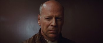 Movie still from “Looper” (2012), directed by Rian Johnson – A man with a bald head and a smirk on his face; Close Up shot, Low angle