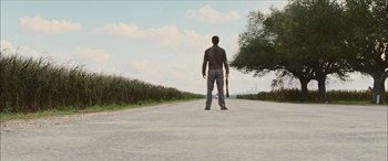 Movie still from “Looper” (2012), directed by Rian Johnson – A man standing on the side of a road holding a skateboard; Extreme Wide shot, Low angle
