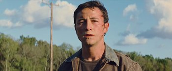 Movie still from “Looper” (2012), directed by Rian Johnson – A young man with a bruised face is standing in front of power lines; Close Up shot, Low angle