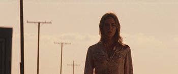 Movie still from “Looper” (2012), directed by Rian Johnson – A woman standing in front of power lines on a sunny day; Medium shot, Low angle