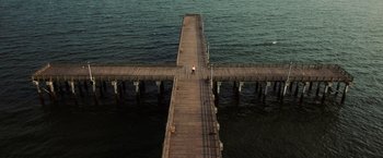 Movie still from “Lord of War” (2005), directed by Andrew Niccol – An aerial view of a person walking on a pier; Extreme Wide shot, Overhead angle