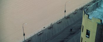 Movie still from “Lord of War” (2005), directed by Andrew Niccol – Two people walking on a boardwalk near the water; Extreme Wide shot, Overhead angle