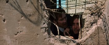 Movie still from “Lord of War” (2005), directed by Andrew Niccol – Two men are talking on a cell phone in front of barbed wire; Close Up shot, Low angle