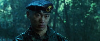 Movie still from “Lord of War” (2005), directed by Andrew Niccol – A man in a military uniform standing next to a forest; Close Up shot, Low angle