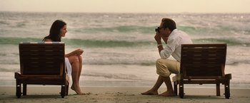 Movie still from “Lord of War” (2005), directed by Andrew Niccol – A man taking a picture of a woman sitting on the beach; Medium shot, Over the shoulder angle