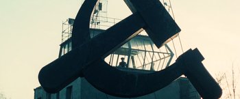Movie still from “Lord of War” (2005), directed by Andrew Niccol – A man standing in front of a large metal sculpture; Extreme Wide shot, Low angle
