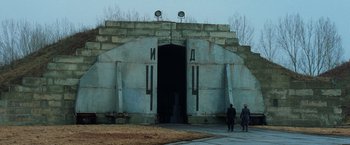 Movie still from “Lord of War” (2005), directed by Andrew Niccol – Two people are standing outside of a building; Extreme Wide shot, Low angle