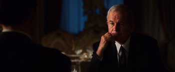 Movie still from “Lord of War” (2005), directed by Andrew Niccol – An older man sitting at a table with a glass of wine in front of him; Close Up shot, Over the shoulder angle