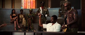 Movie still from “Lord of War” (2005), directed by Andrew Niccol – A man sitting in a chair in front of a soldier; Medium shot, Low angle
