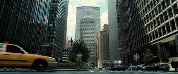 Movie still from “Lord of War” (2005), directed by Andrew Niccol – A man standing on the side of a road in front of tall buildings; Extreme Wide shot, High angle
