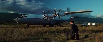 Movie still from “Lord of War” (2005), directed by Andrew Niccol – A man sitting on a chair in front of an airplane in a field; Wide shot, Low angle