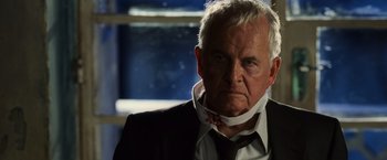 Movie still from “Lord of War” (2005), directed by Andrew Niccol – An older man wearing a neck brace and a suit; Close Up shot, Low angle