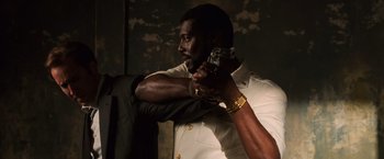 Movie still from “Lord of War” (2005), directed by Andrew Niccol – A man in a white shirt holding a gun in his hand; Medium shot, Over the shoulder angle