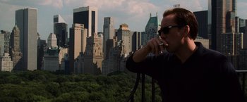 Movie still from “Lord of War” (2005), directed by Andrew Niccol – A man standing on top of a building eating food; Medium shot, Low angle