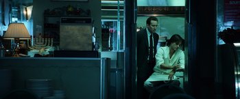 Movie still from “Lord of War” (2005), directed by Andrew Niccol – A man and a woman sitting at a table in front of a counter; Medium shot, Over the shoulder angle