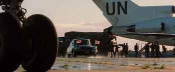 Movie still from “Lord of War” (2005), directed by Andrew Niccol – A car driving down a road next to an air force plane; Extreme Wide shot, Low angle