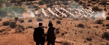 Movie still from “Lord of War” (2005), directed by Andrew Niccol – Two people standing in the desert looking at tents in the background; Wide shot, High angle