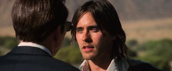 Movie still from “Lord of War” (2005), directed by Andrew Niccol – A man with long black hair is looking at the camera; Close Up shot, Over the shoulder angle