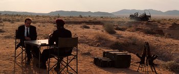 Movie still from “Lord of War” (2005), directed by Andrew Niccol – A man sitting in a chair in the middle of the desert; Wide shot, Over the shoulder angle