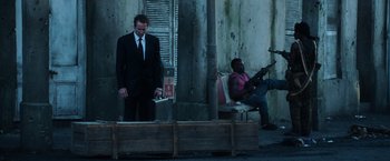 Movie still from “Lord of War” (2005), directed by Andrew Niccol – A man in a suit and tie holding a briefcase; Wide shot, Over the shoulder angle