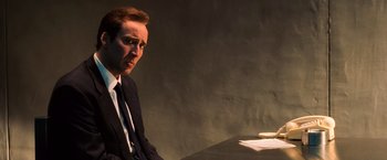 Movie still from “Lord of War” (2005), directed by Andrew Niccol – A man in a suit and tie sitting at a table; Close Up shot, Low angle