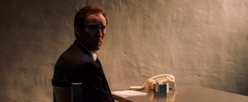 Movie still from “Lord of War” (2005), directed by Andrew Niccol – A man sitting at a table in front of a phone; Close Up shot, Low angle