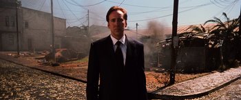 Movie still from “Lord of War” (2005), directed by Andrew Niccol – A man wearing a suit and tie standing in front of a train track; Medium shot, Low angle
