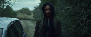 Movie still from “Lost Bullet 2: Back for More” (2022), directed by Guillaume Pierret – A woman with dreadlocks standing on the side of a road; Medium shot, Low angle