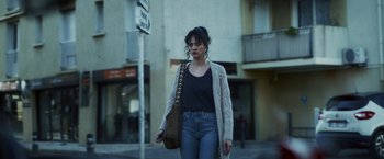 Movie still from “Lost Bullet 2: Back for More” (2022), directed by Guillaume Pierret – A woman walking down the street holding a purse; Medium shot, Low angle
