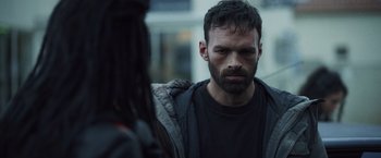 Movie still from “Lost Bullet 2: Back for More” (2022), directed by Guillaume Pierret – A man with long hair and a beard looking at another man; Close Up shot, Over the shoulder angle