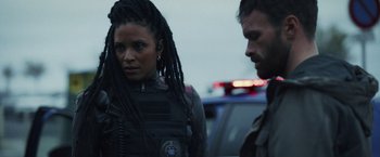 Movie still from “Lost Bullet 2: Back for More” (2022), directed by Guillaume Pierret – A man and a woman standing next to a police car; Close Up shot, Over the shoulder angle