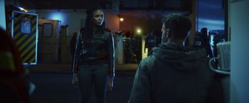 Movie still from “Lost Bullet 2: Back for More” (2022), directed by Guillaume Pierret – A woman standing next to a man in a dark room; Medium shot, Over the shoulder angle