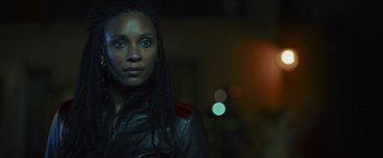 Movie still from “Lost Bullet 2: Back for More” (2022), directed by Guillaume Pierret – A woman with dreadlocks wearing a leather jacket; Close Up shot, Over the shoulder angle