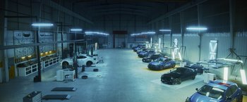 Movie still from “Lost Bullet 2: Back for More” (2022), directed by Guillaume Pierret – A garage filled with lots of cars parked on top of the floor; Extreme Wide shot, High angle