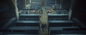 Movie still from “Lost Bullet 2: Back for More” (2022), directed by Guillaume Pierret – Two people walking through a room with a lot of shelves; Extreme Wide shot, High angle