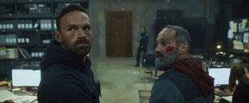 Movie still from “Lost Bullet 2: Back for More” (2022), directed by Guillaume Pierret – A couple of men standing next to each other in a room; Medium shot, Over the shoulder angle